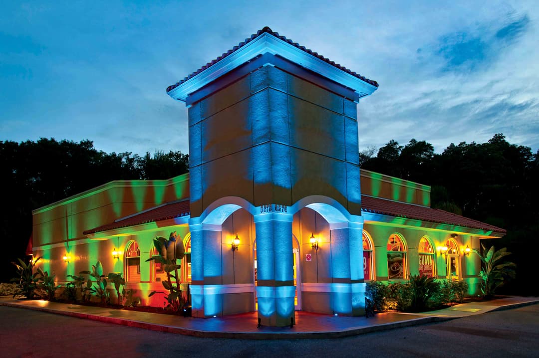 Vibrantly lit restaurant exterior at dusk with colorful blue and green lights.