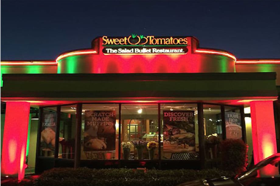 Sweet Tomatoes restaurant illuminated at night, showcasing a colorful exterior and lighted signage.