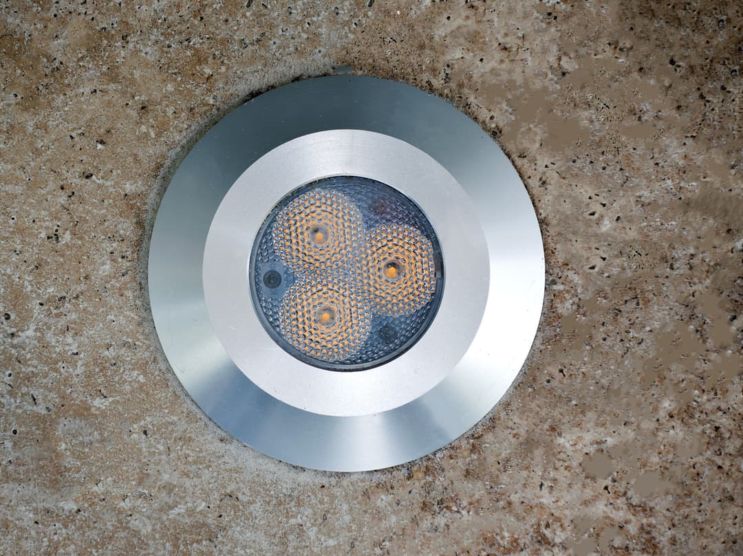 LED outdoor wall light fixture with three illuminated bulbs on a textured surface.