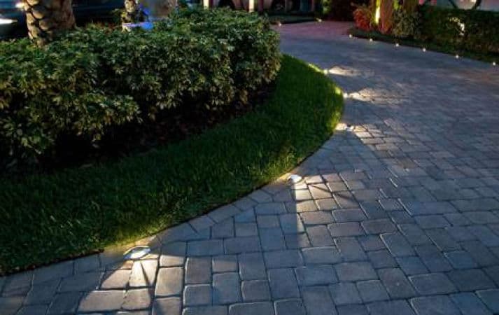 Pathway with stone pavers and low-profile lighting along the curved edge of green grass.