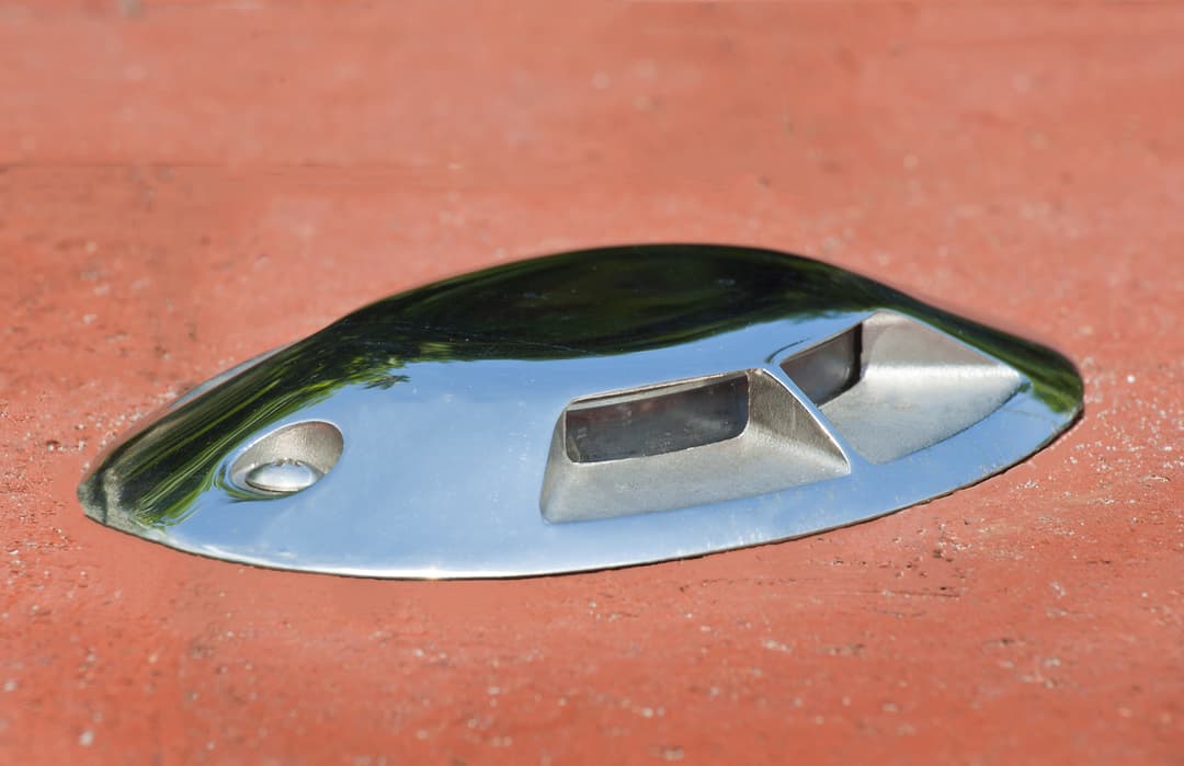 Metallic reflective marker on a red surface, commonly used for navigation or as a trail marker.