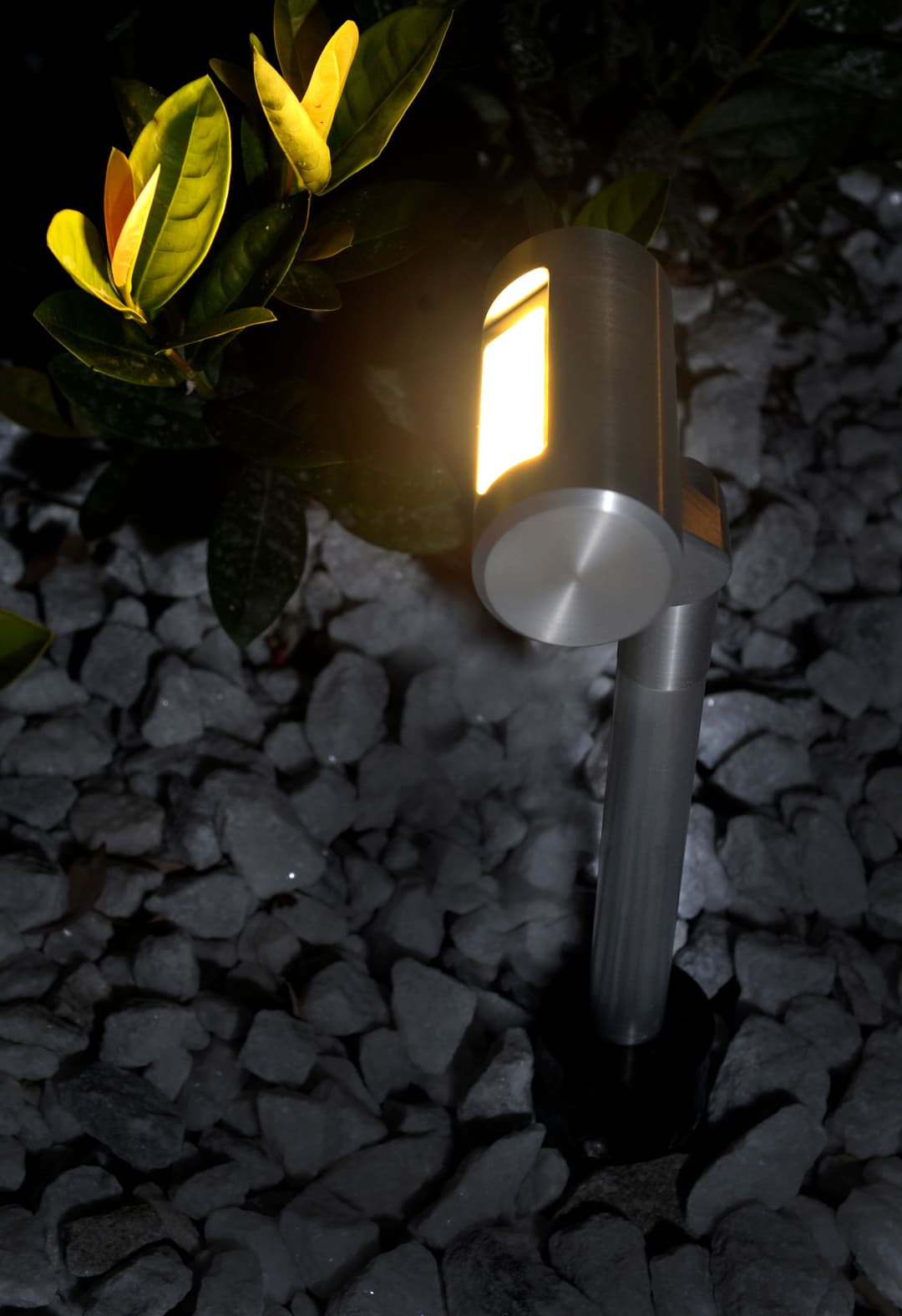 Solar garden light illuminating plants on gravel landscape at night.