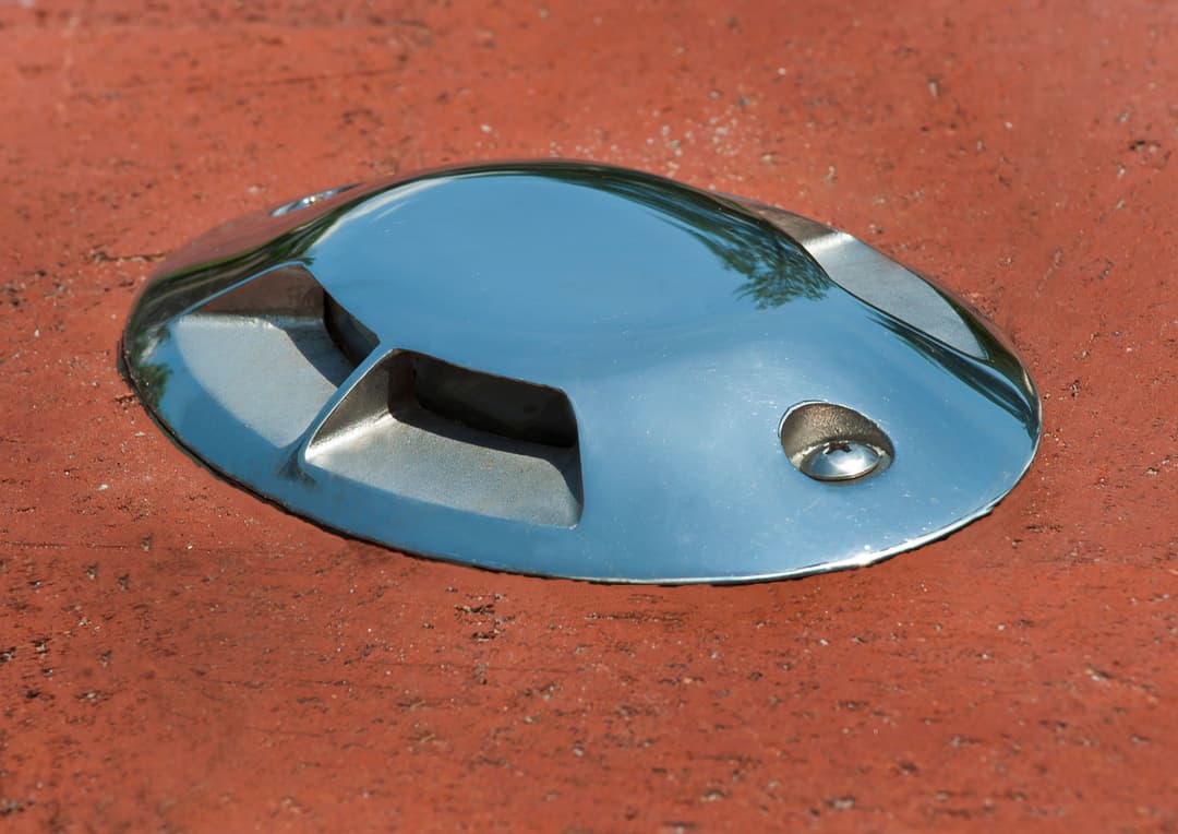 Close-up of a shiny metal object on a textured red surface, reflecting greenery above.