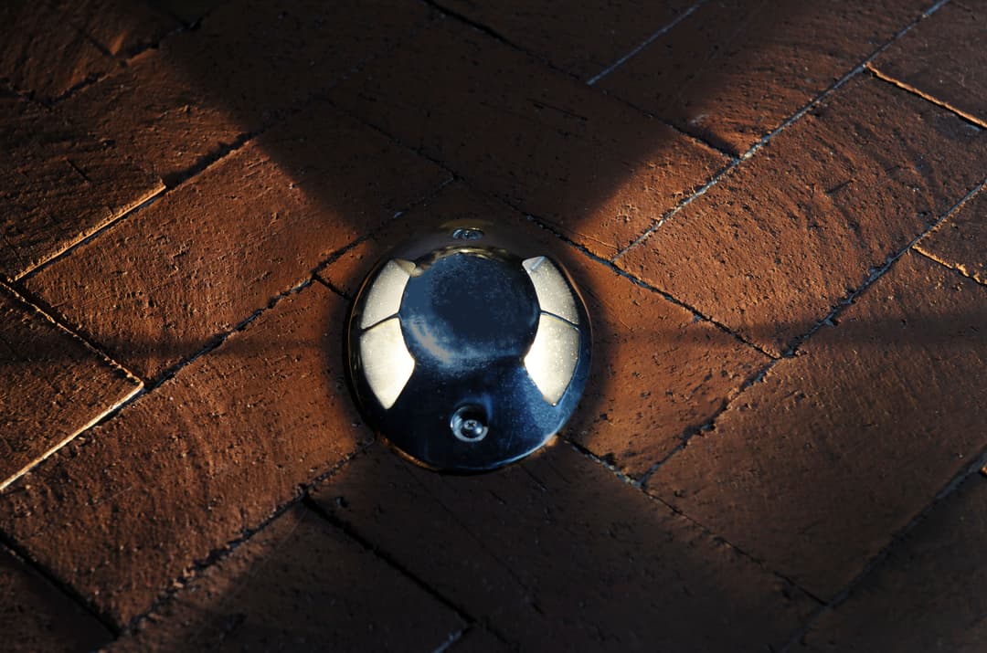 Metal floor marker on textured brick surface, casting shadows in ambient light.