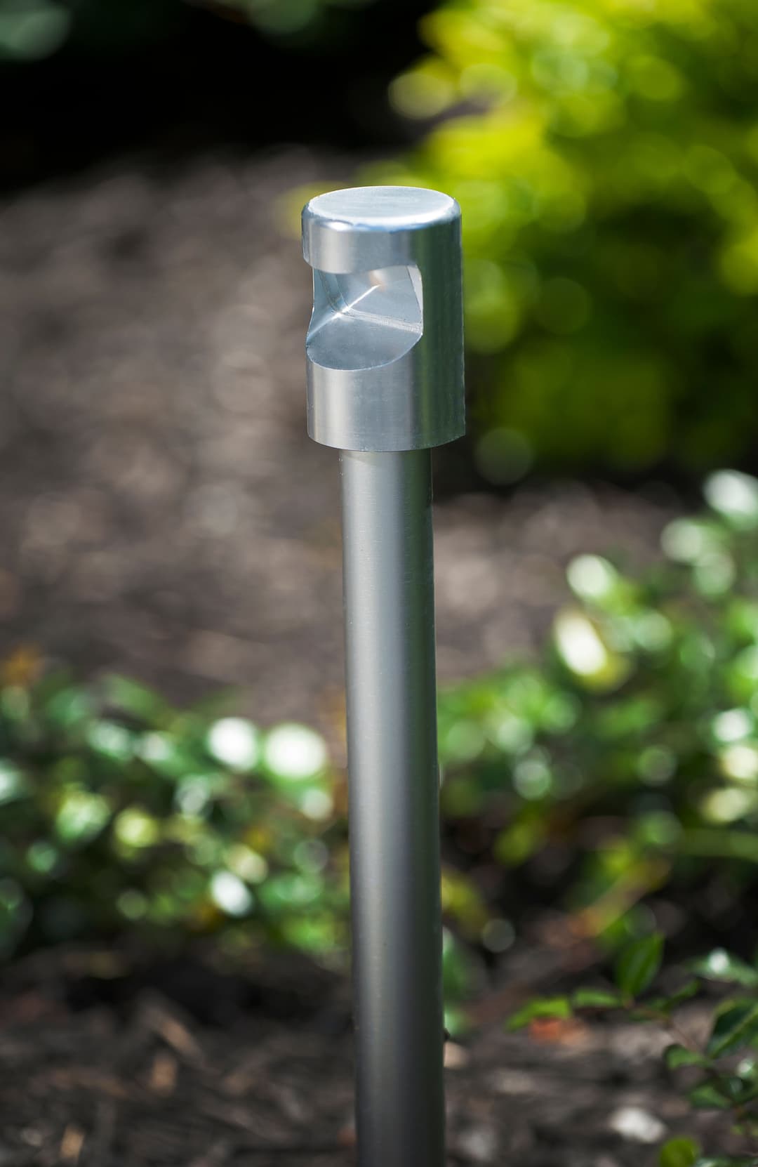 Metal landscape stake with a circular top, set against a blurred green background.