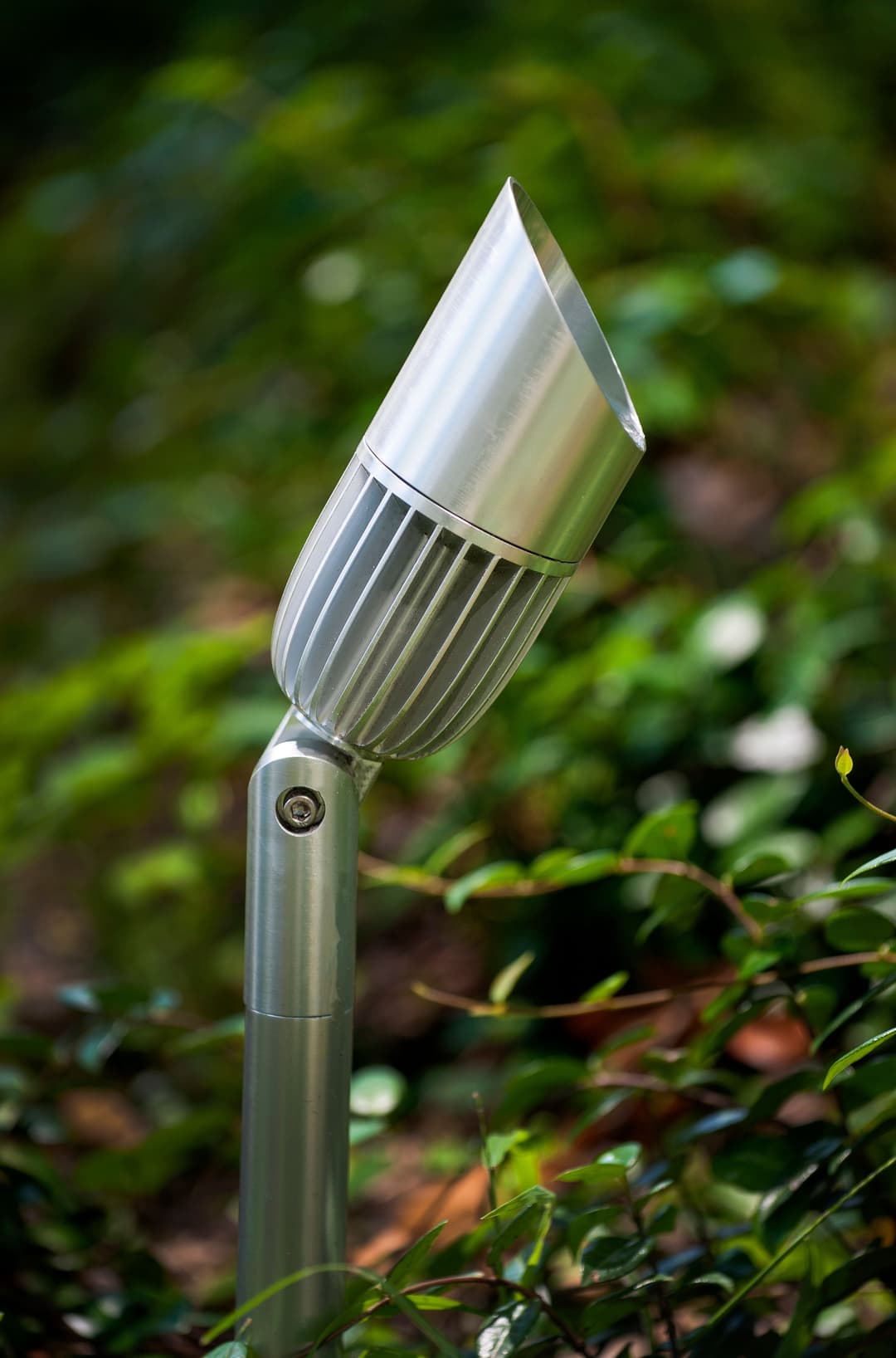 Sleek silver outdoor spotlight on a green shrub, enhancing landscape illumination.